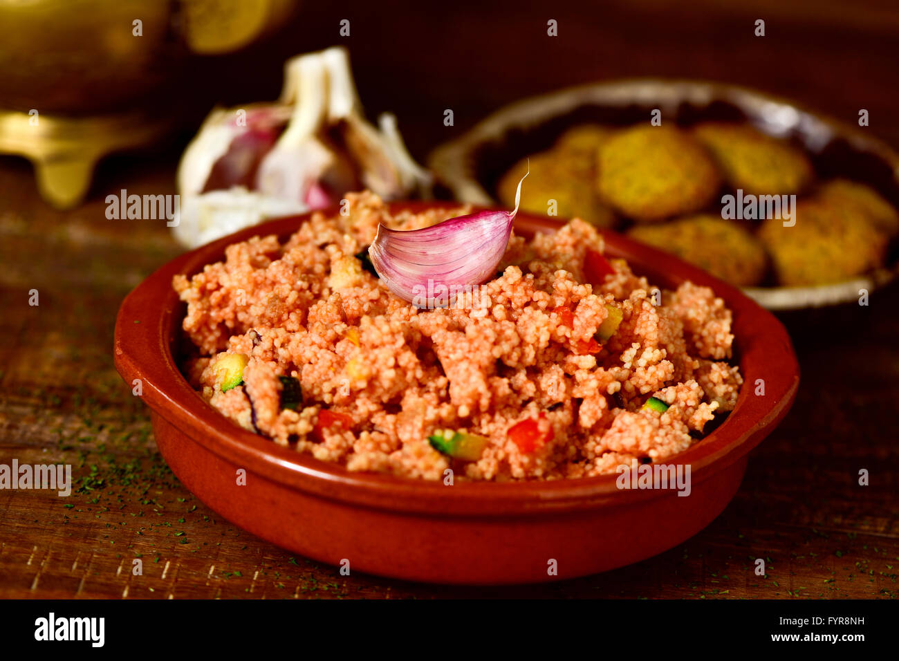 closeup of an earthenware casserole whit couscous with vegetables and some falafel in a plate in the background, on a wooden tab Stock Photo