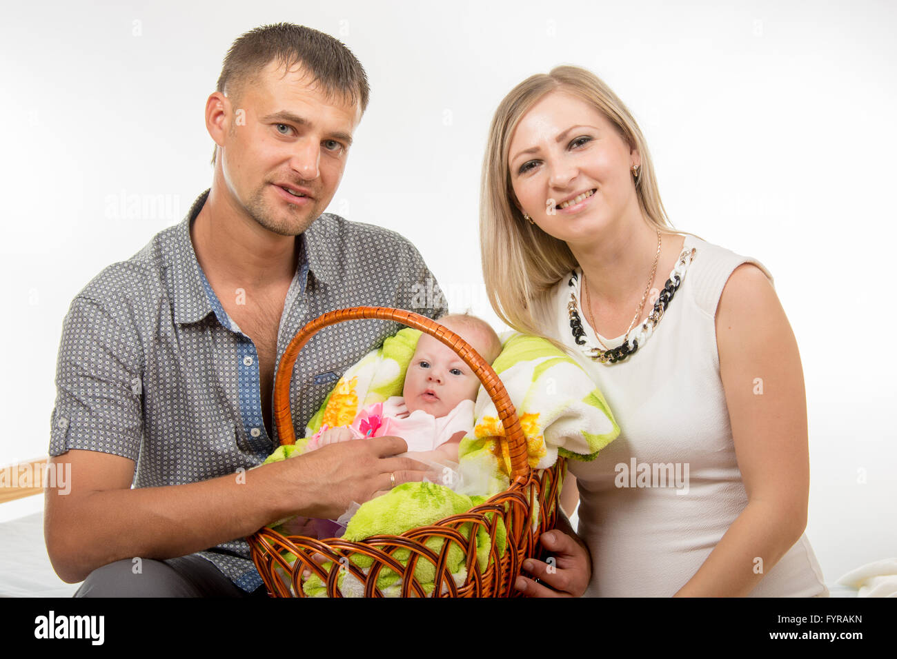 Mom and dad sit on the bed and holding a two-month baby girl in a basket Stock Photo