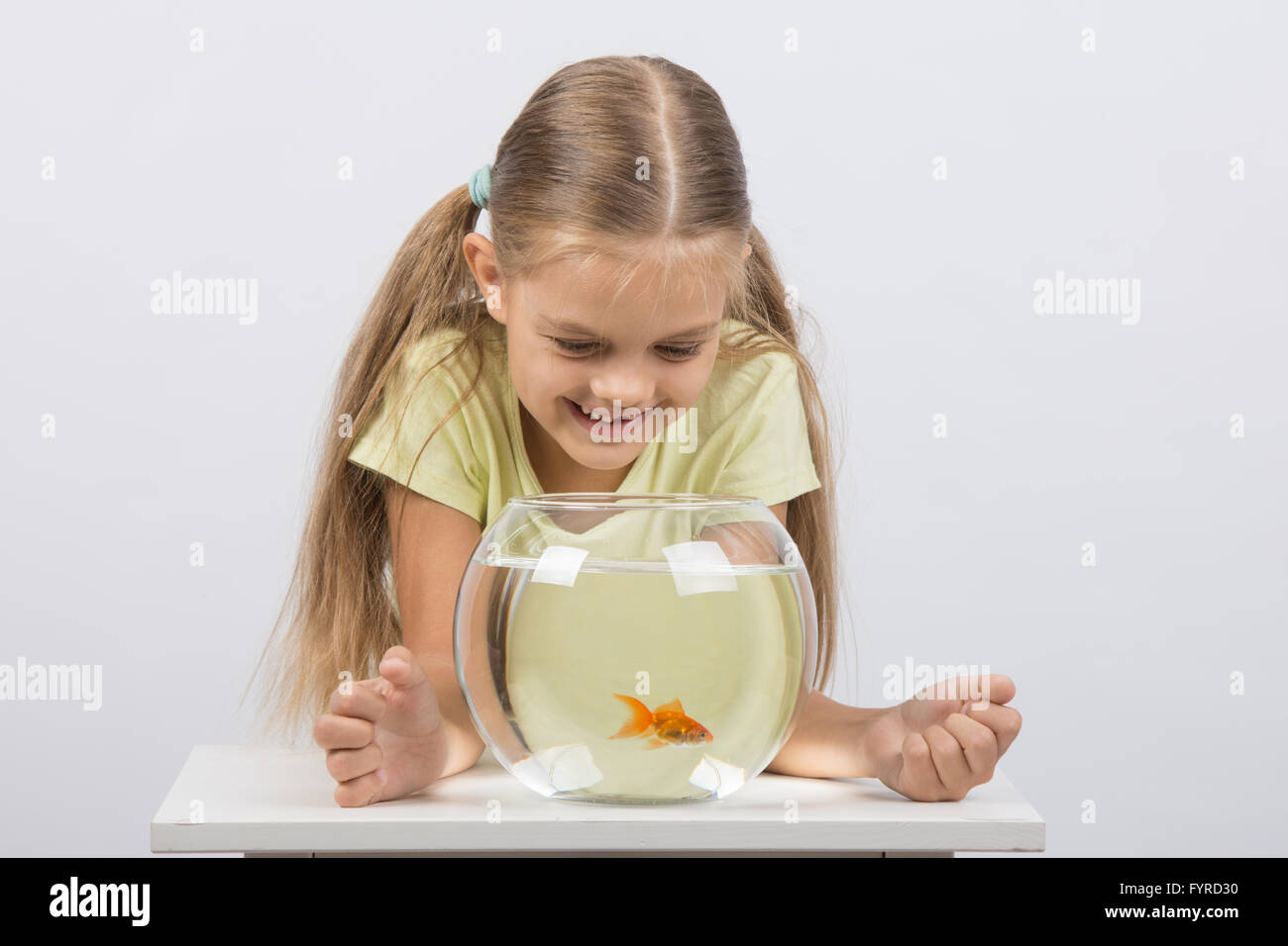 Happy six year old girl looking down on the aquarium with goldfish Stock Photo