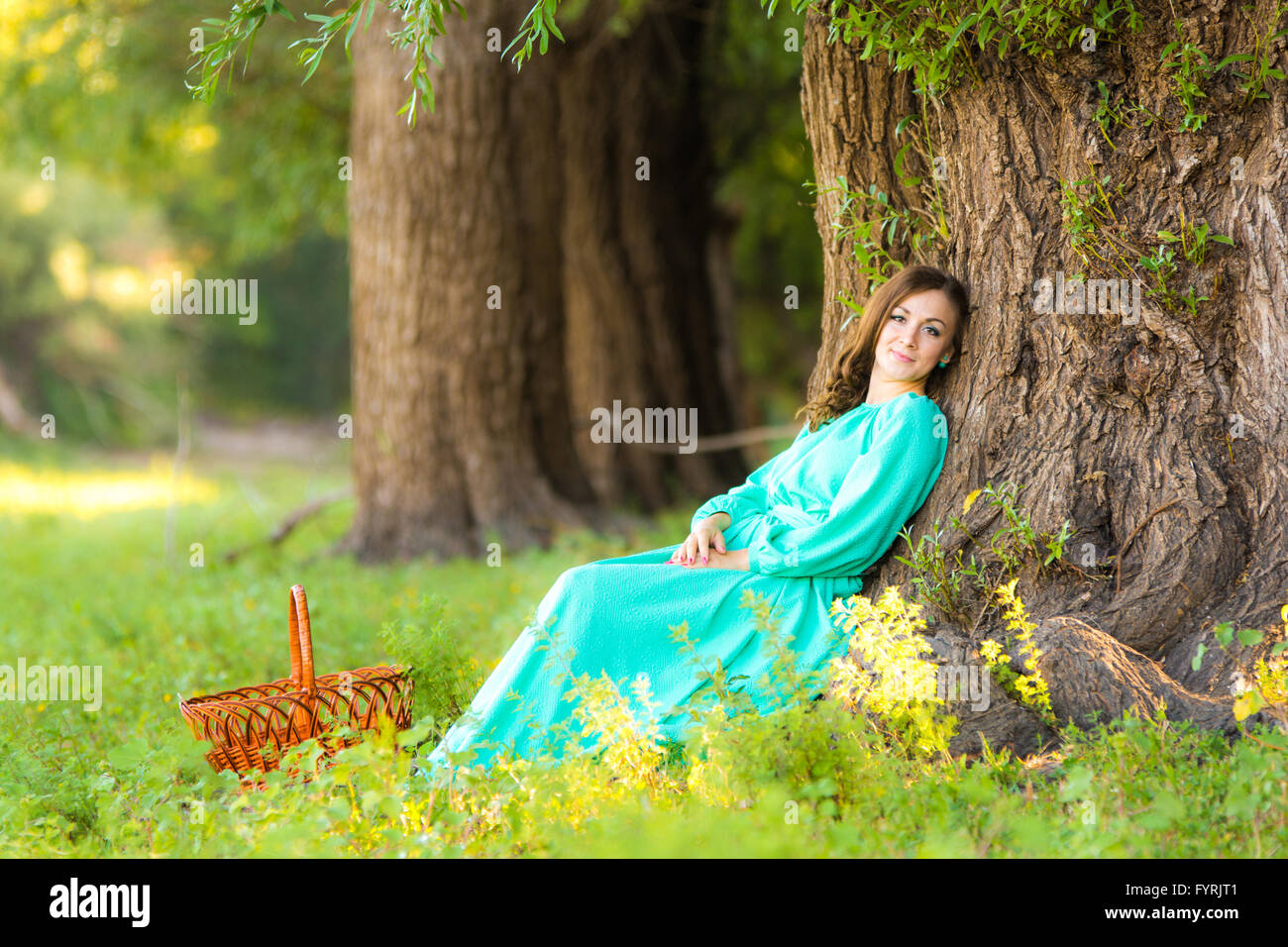 A girl in a long dress and sat resting at a big tree in the forest ...