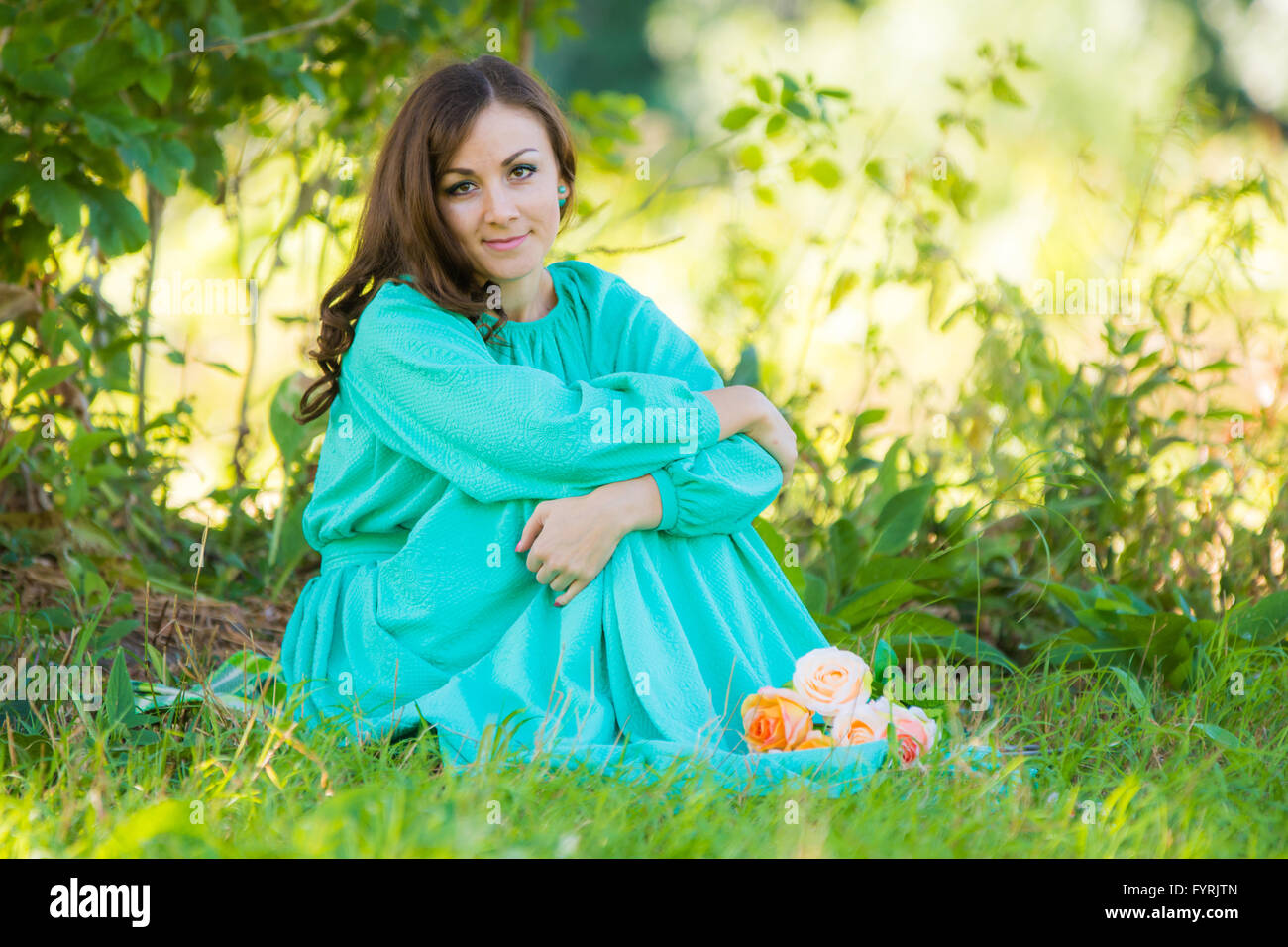 A girl in a long dress sitting in the shade of the trees on a sunny day ...