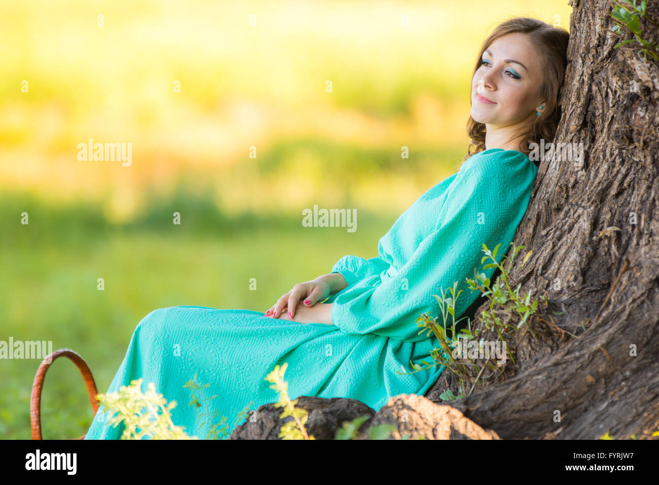 A girl in a long dress and sat resting at a big tree in the forest ...