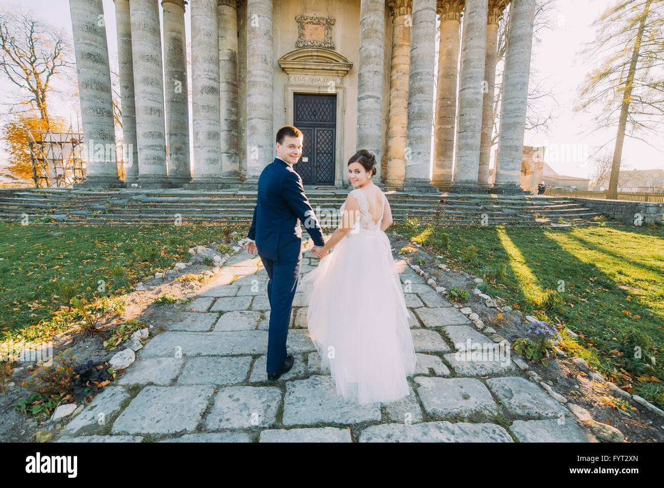 Beautiful bride and groom walking holding hands in front of old ...