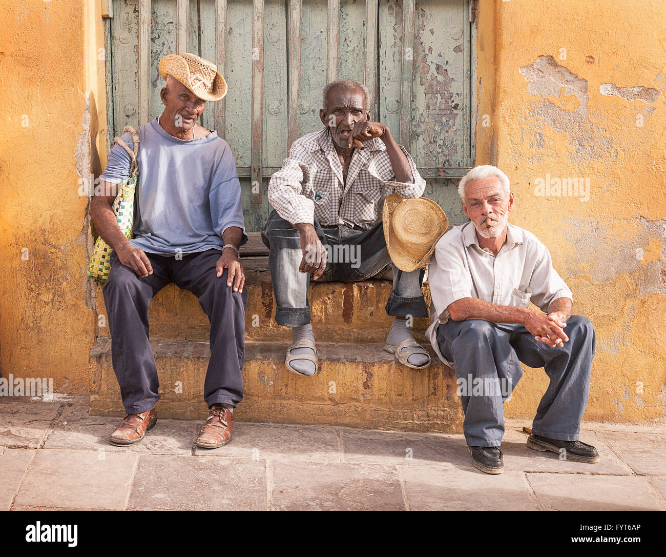 The Three Amigos. Three men sitting together on a doorstep in Trinidad, Cuba. They seem to be old retired friends passing the time in the sunshine. Stock Photo