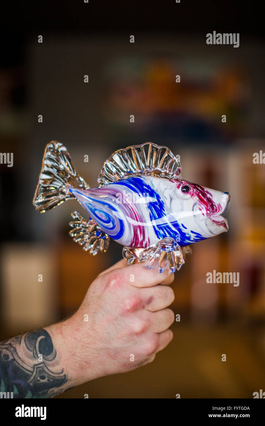 A man holds a glass sculpture of a fish in his hand at a glass blowing