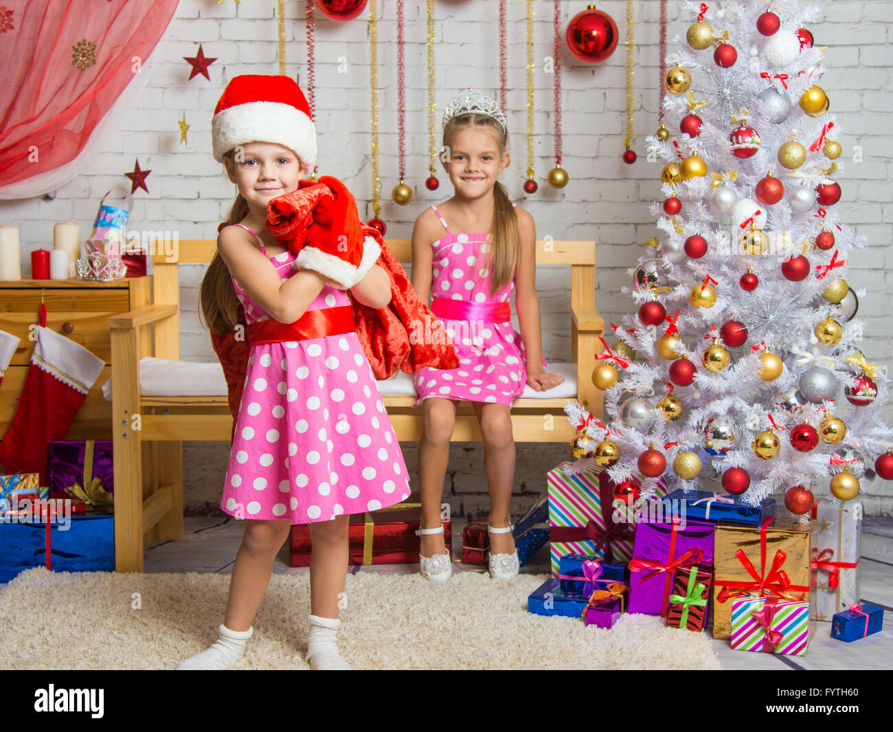 Girl dressed as Santa Claus brought gifts in the bag, another girl rejoices Stock Photo