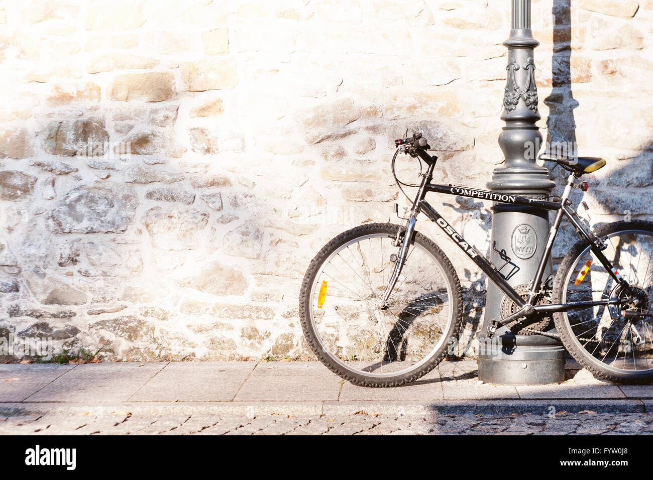 Bicycle leaning on a lamppost in the sun casting shadow on the stone wall Stock Photo
