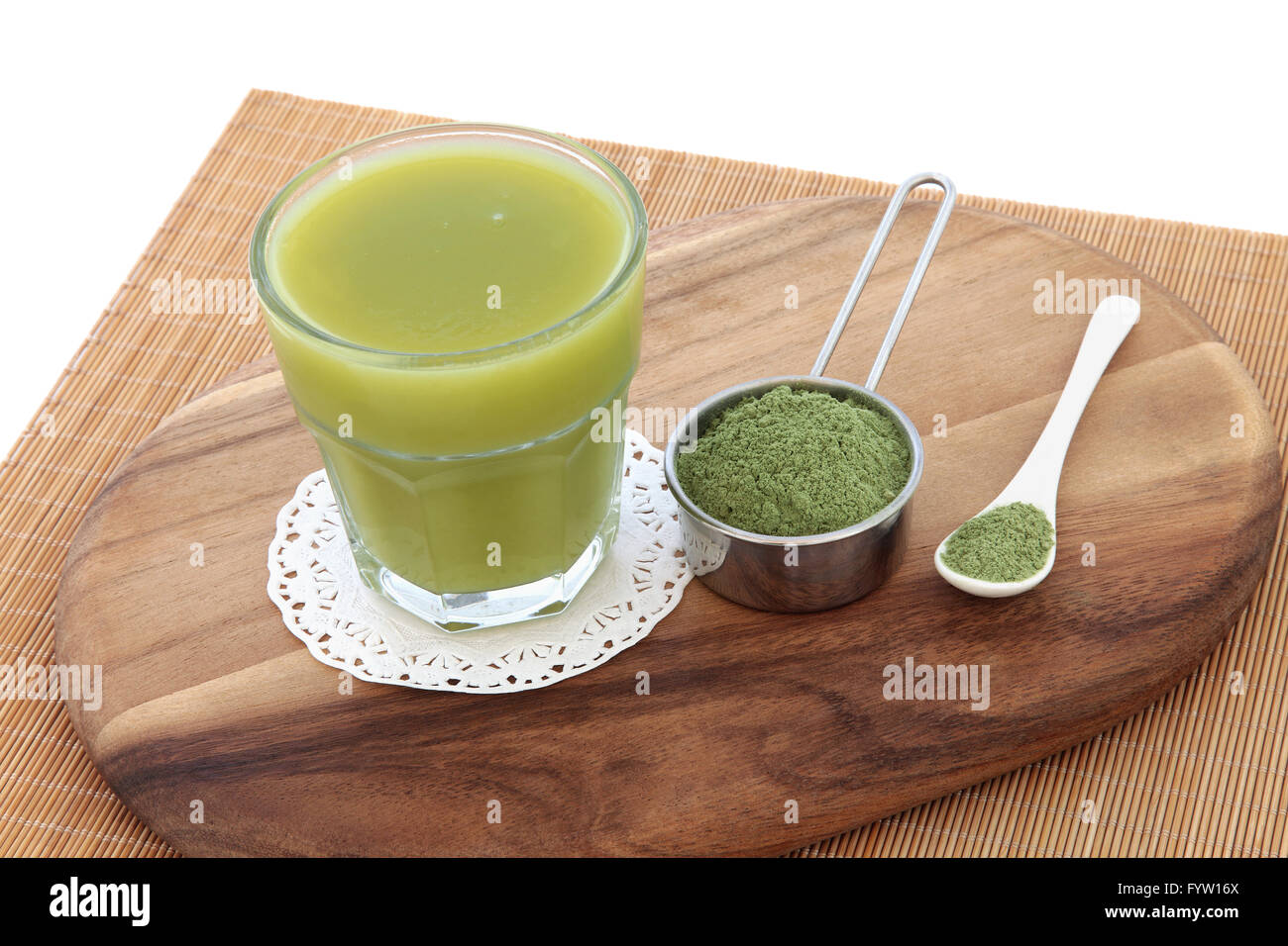 Wheat grass health drink with powder in scoop and spoon on a maple wood board over bamboo and white background. Stock Photo