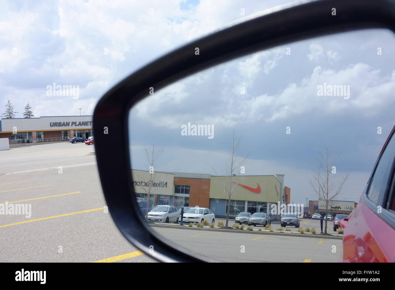 The Nike logo is reflected in the wing mirror of a car parked in a large  shopping car park Stock Photo - Alamy