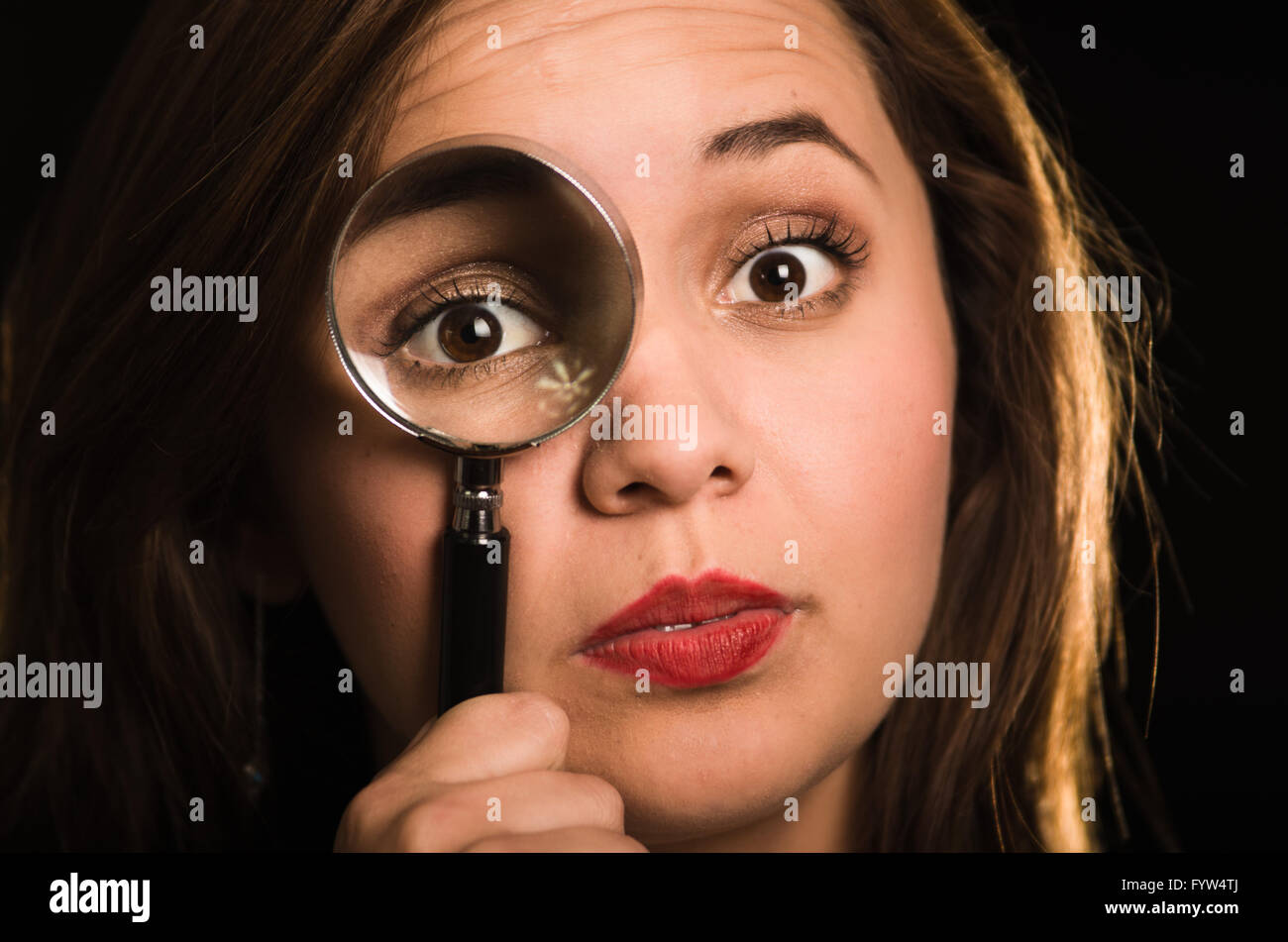 Young woman facing camera holding magnifying glass over right eye