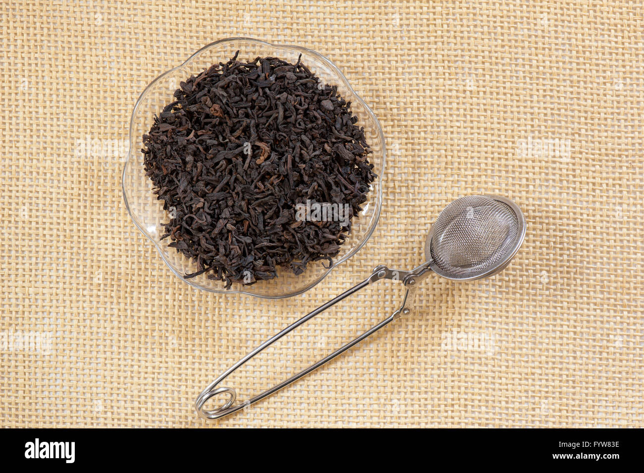 Pu erh dried leaves portion lying on glass saucer and empty metal mesh tea infuser teaball on mat, dry raw healthy plant foliage Stock Photo
