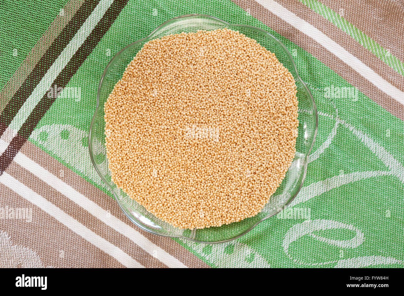Tiny amaranthus grains lying on glass saucer on green cloth, raw product healthy food staple, portion of plant seeds top view. Stock Photo