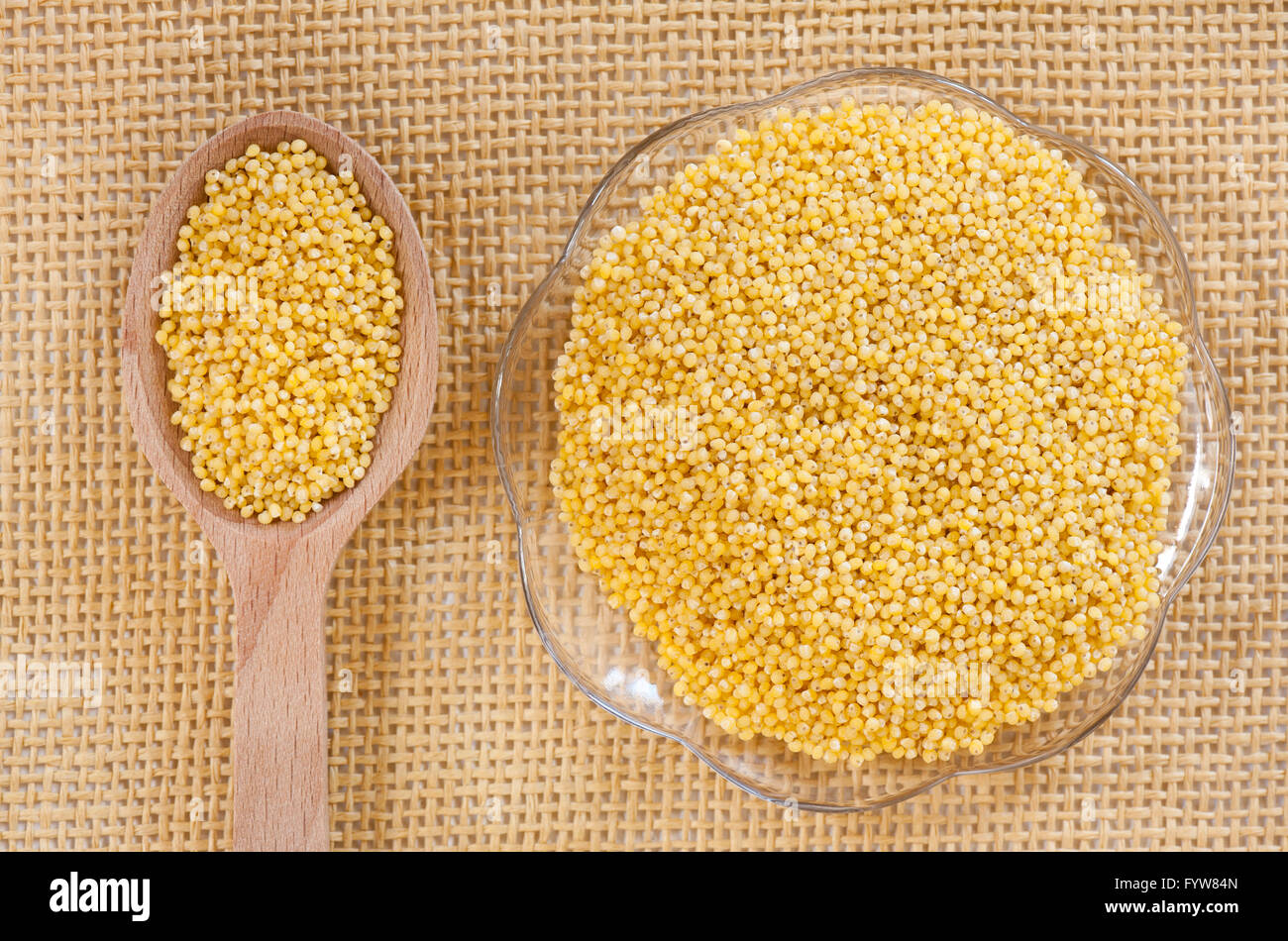 Yellow millet hulled grains lying on glass saucer and wooden spoon on