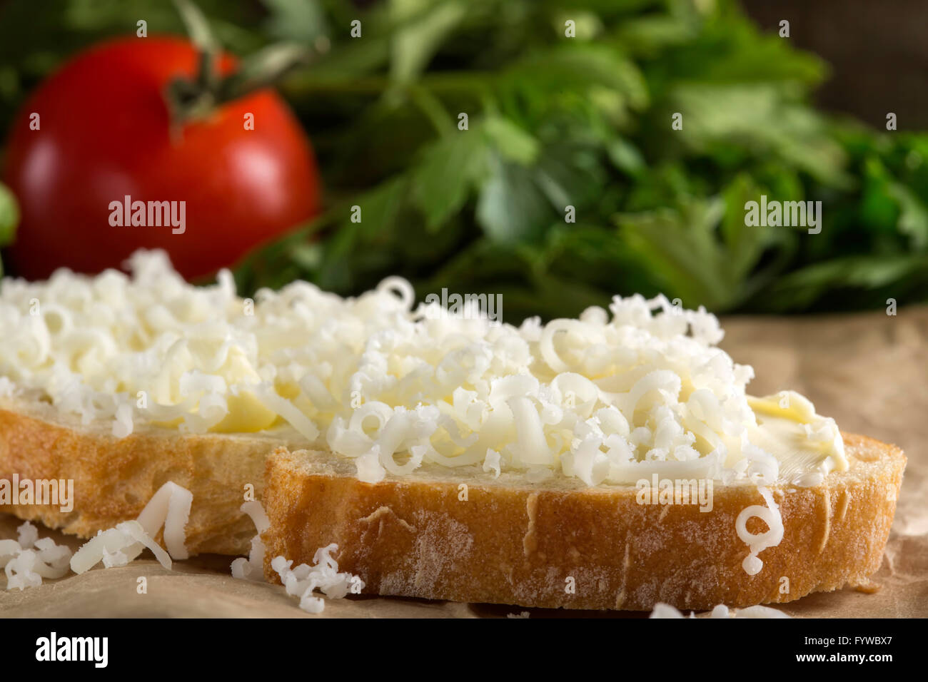 Slice of bread with butter and grated cheese and tomato with parsley in background Stock Photo