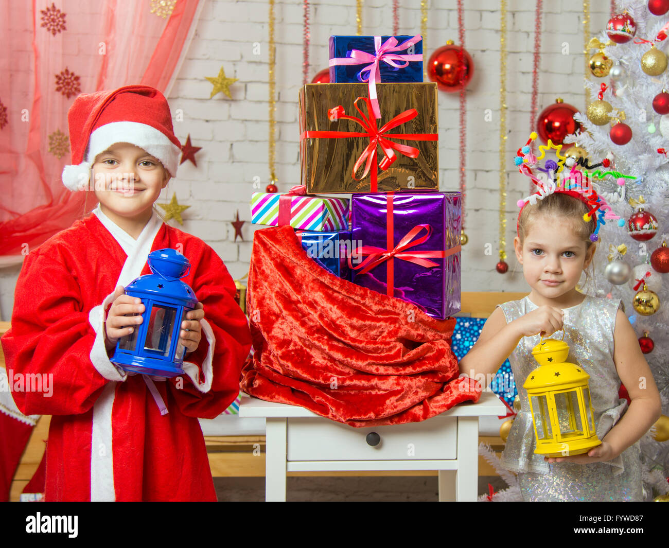 Two girls in Christmas costumes are with candlesticks from the bag with Christmas gifts Stock Photo