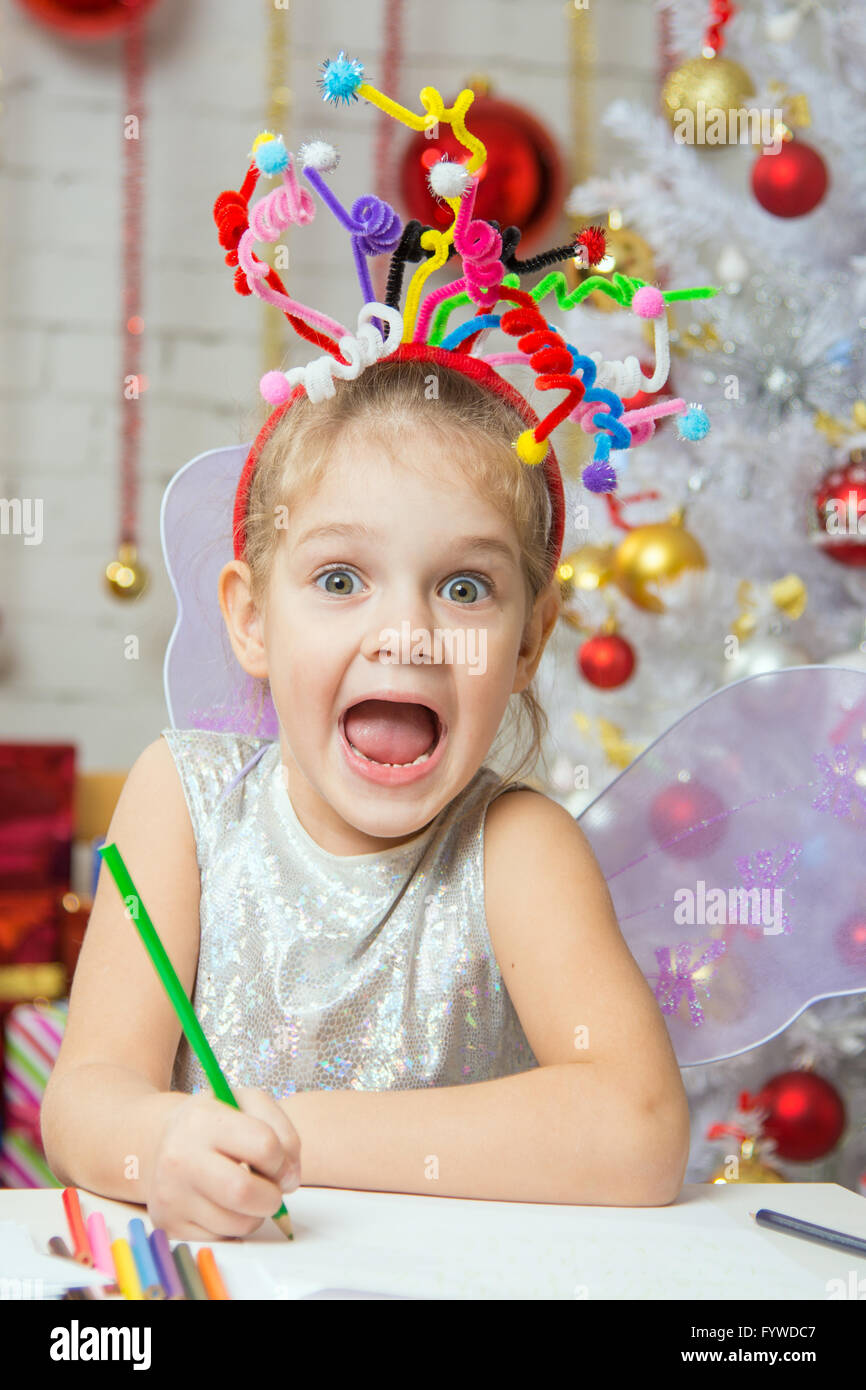 Girl with a toy fireworks on the head draws a congratulatory New Years card Stock Photo