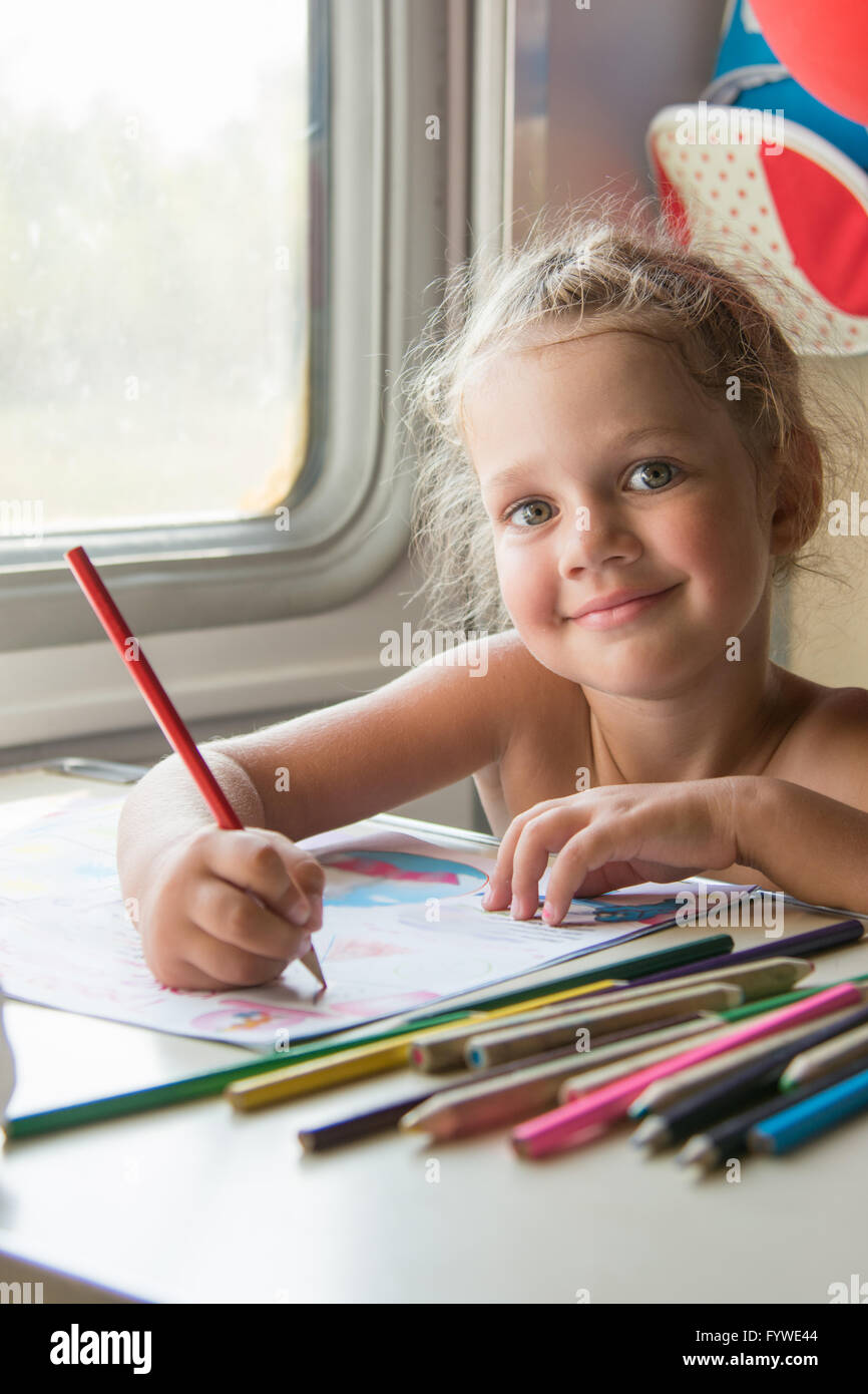 Four-year girl draws pencil drawing of a table in a second-class train carriage Stock Photo