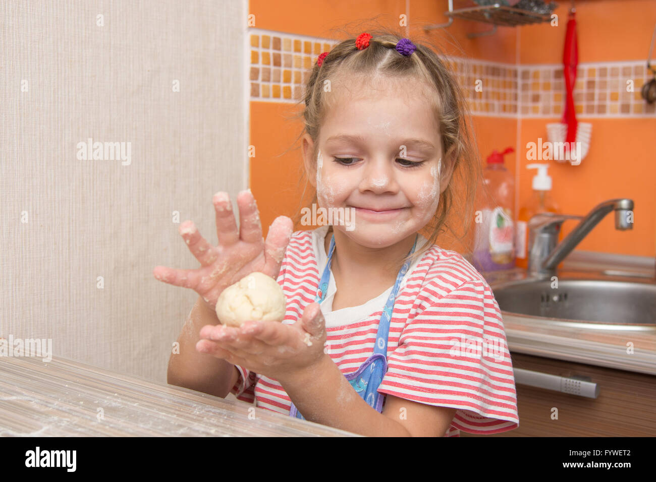 Happy little girl girl sculpts a pie at the kitchen table Stock Photo