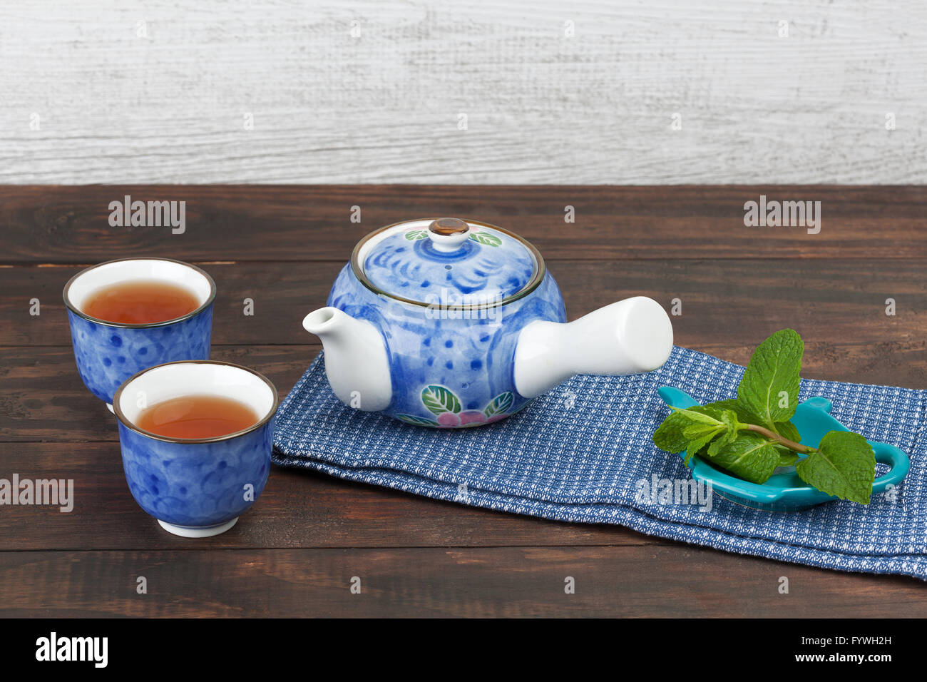 Japanese side-handled teapot with two cups and mint on teatowel and wooden desk with copy space. Stock Photo