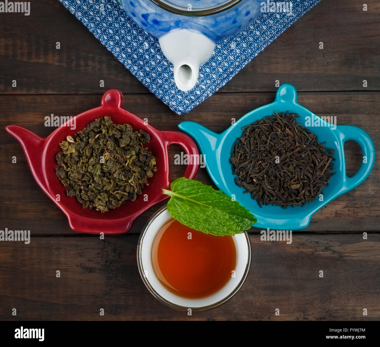 Closeup of teapot, whole leaf tea varieties and teacup with mint leaf on wooden table. Top view. Stock Photo