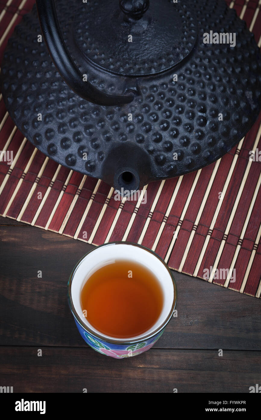 Traditional Japanese cast iron teapot with teacup on bamboo mat