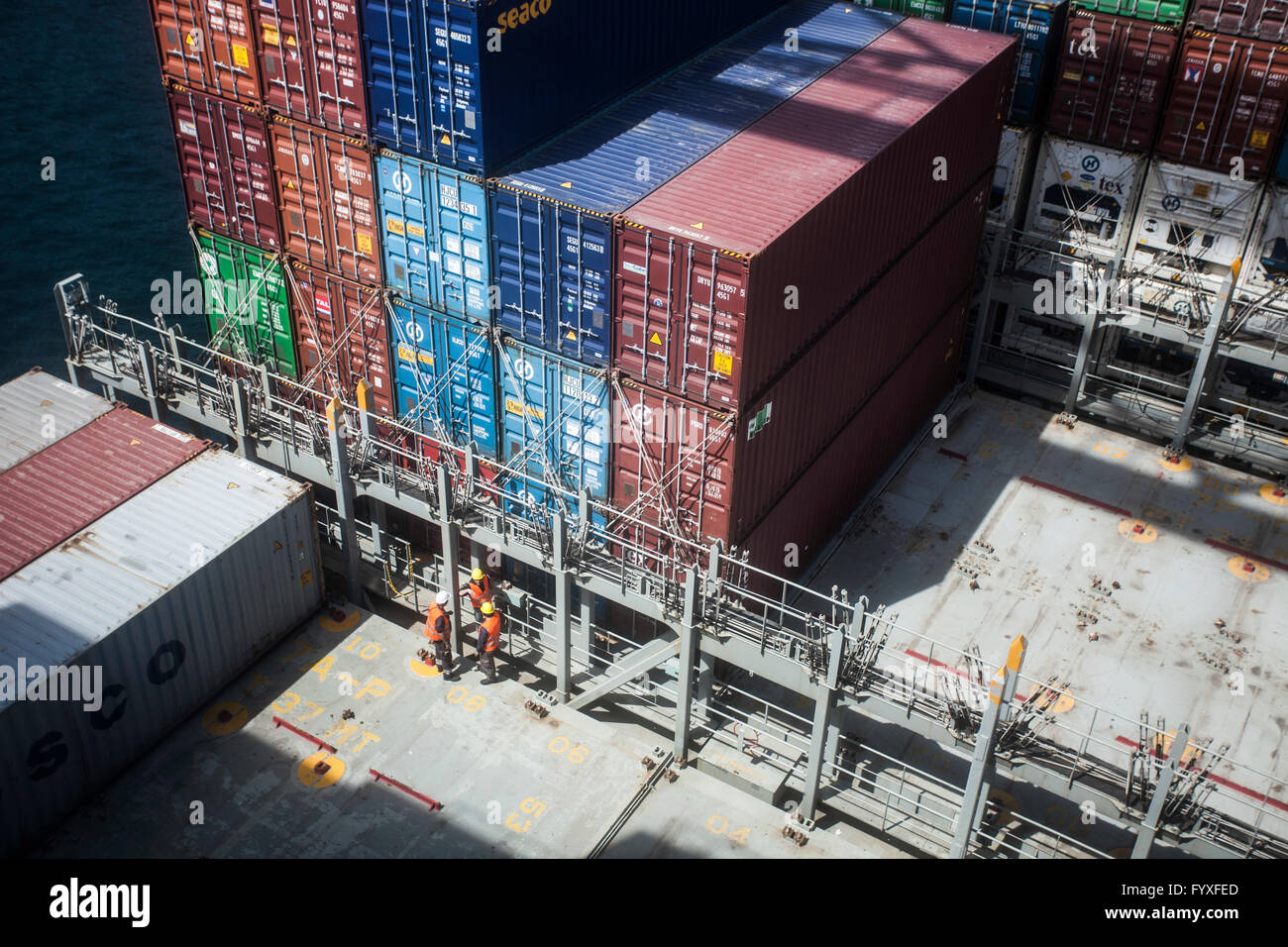Workers on a container ship assisting with the process of stacking containers while docked at port. Stock Photo