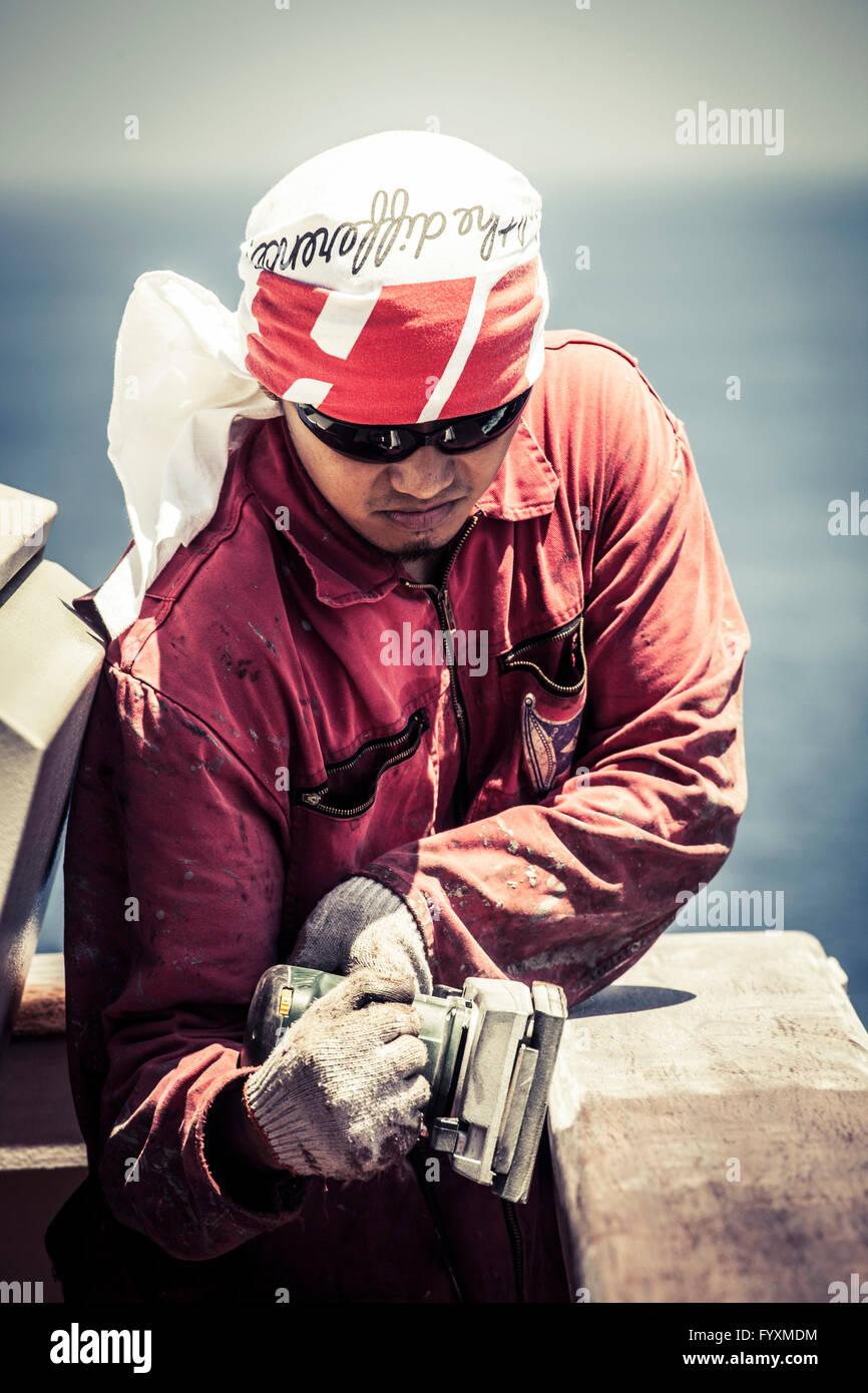 Seaman sanding a railing on a container ship while at sea. Stock Photo