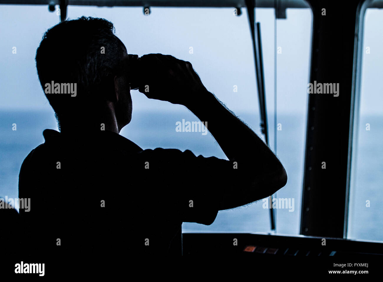 Silhouette of man with binoculars on a container ship at sea Stock Photo