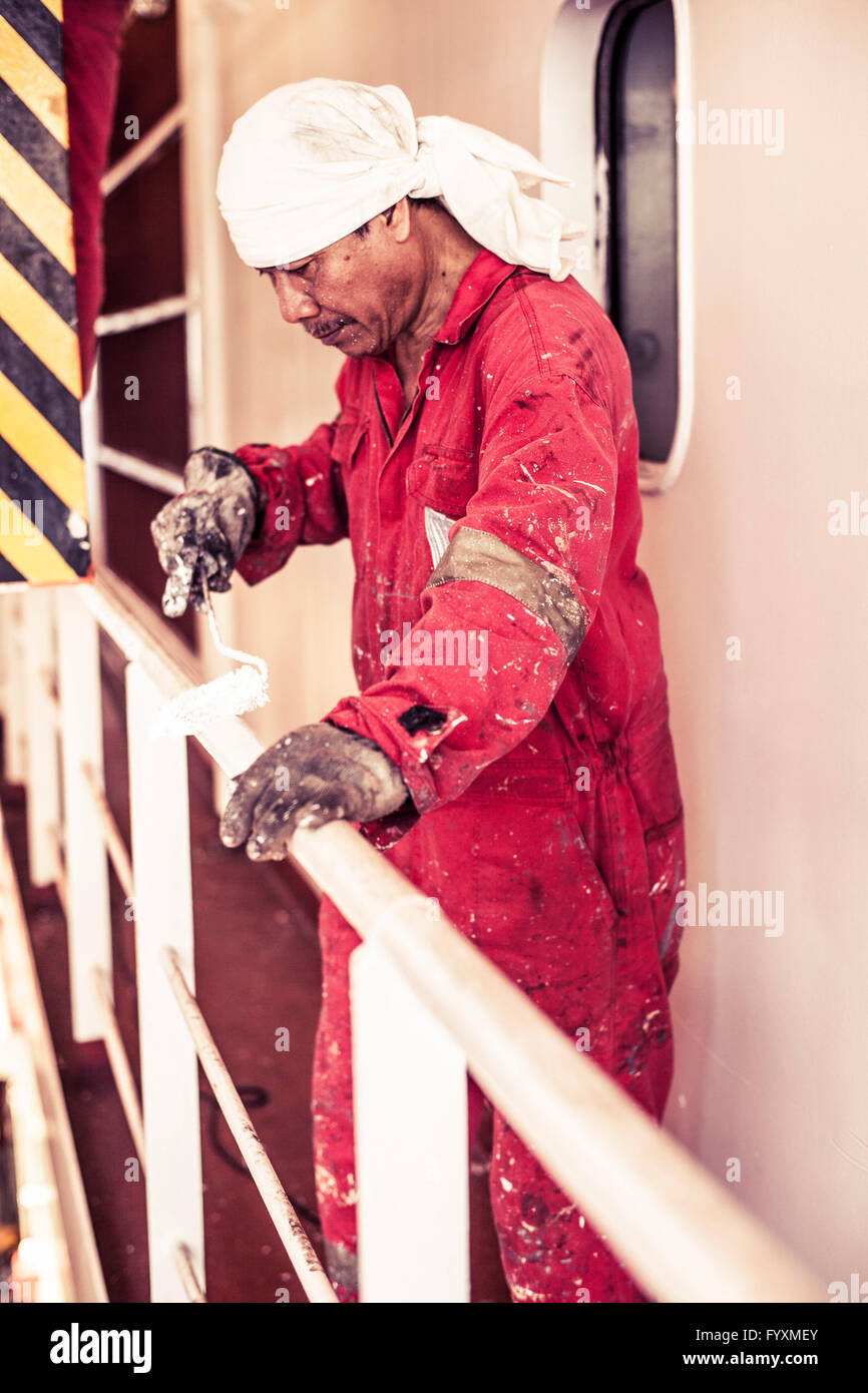Seaman painting railing onboard a container ship at sea. Stock Photo