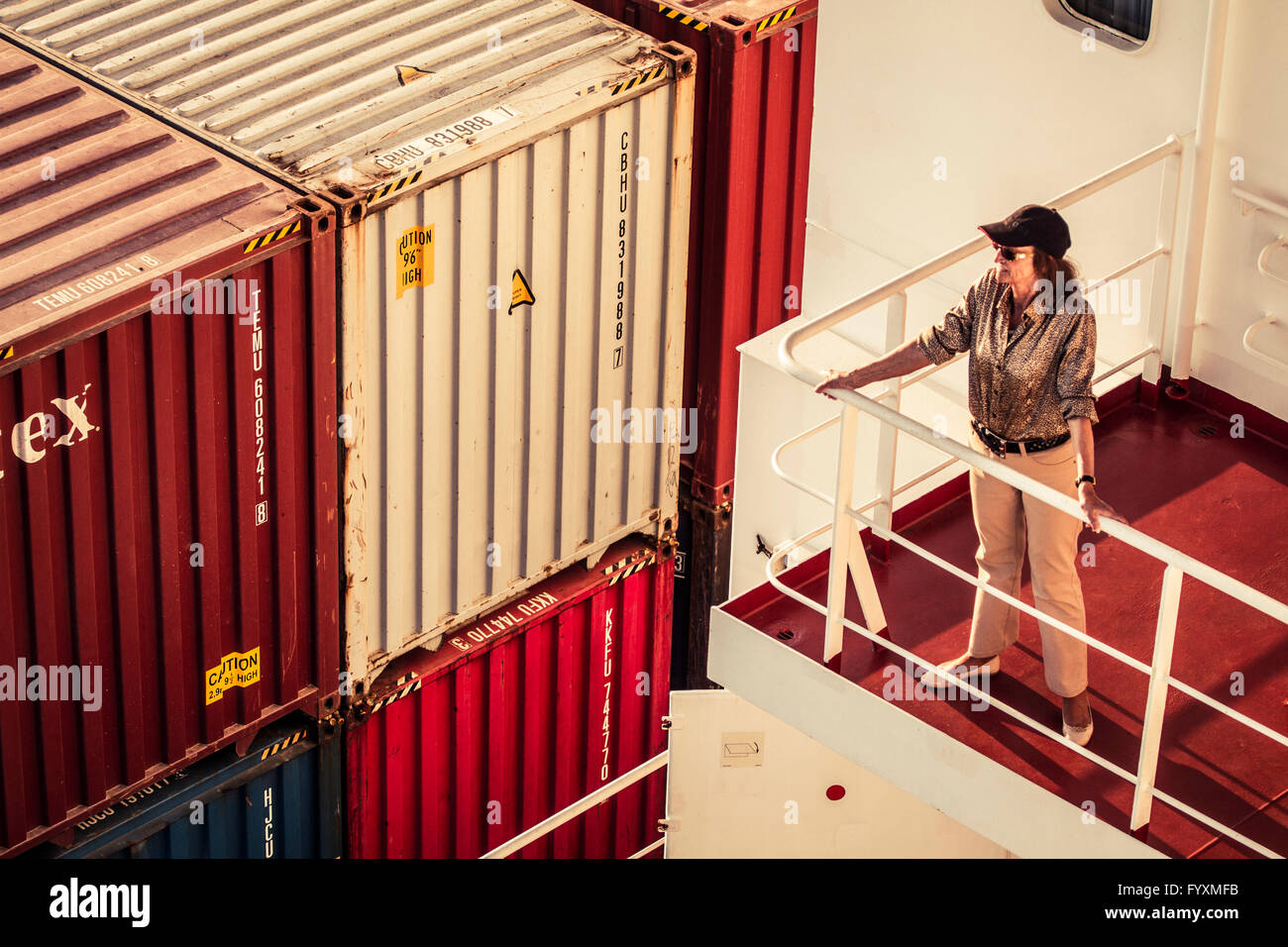 Elderly woman traveler looking towards the sea from one of the living quarters decks on a container ship at sea. Stock Photo
