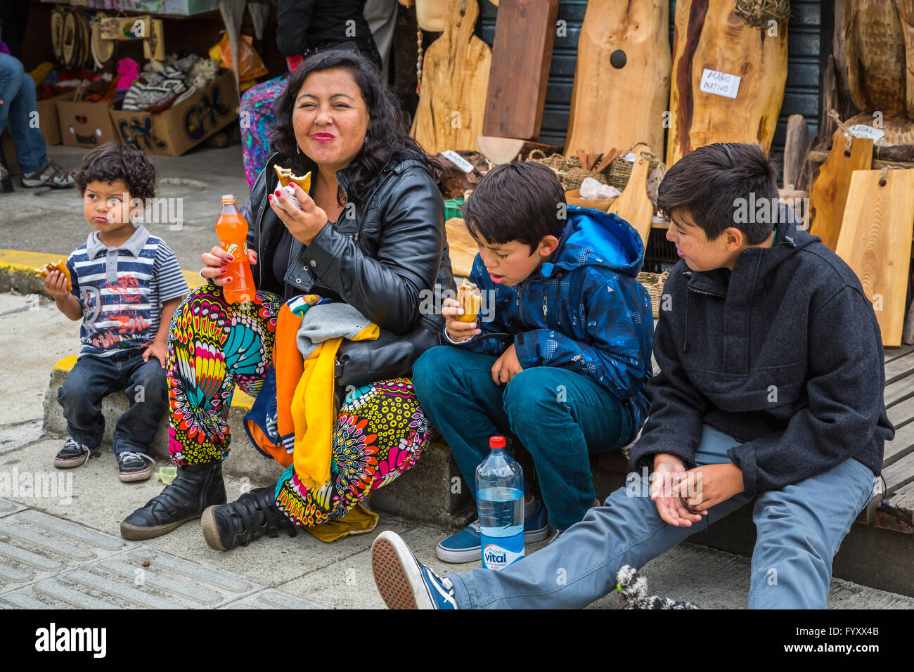 A mother and three boys having and empanada lunch on the sidewalk in Dalcahue, Chile, South America. Stock Photo