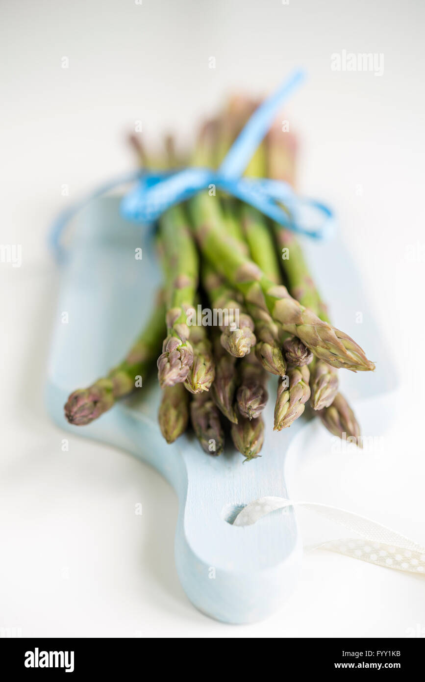 Bunch of fresh asparagus on a blue wooden cutting board with shallow depth of field Stock Photo