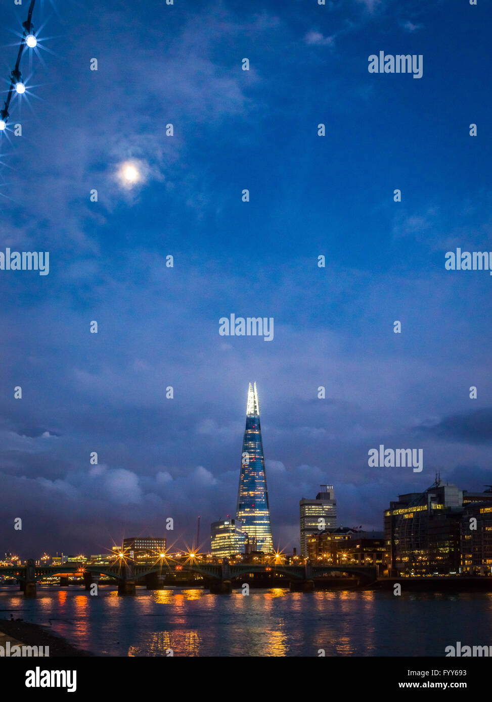 The Shard glows as the moon rises into a cloudy blue twilight sky Stock Photo