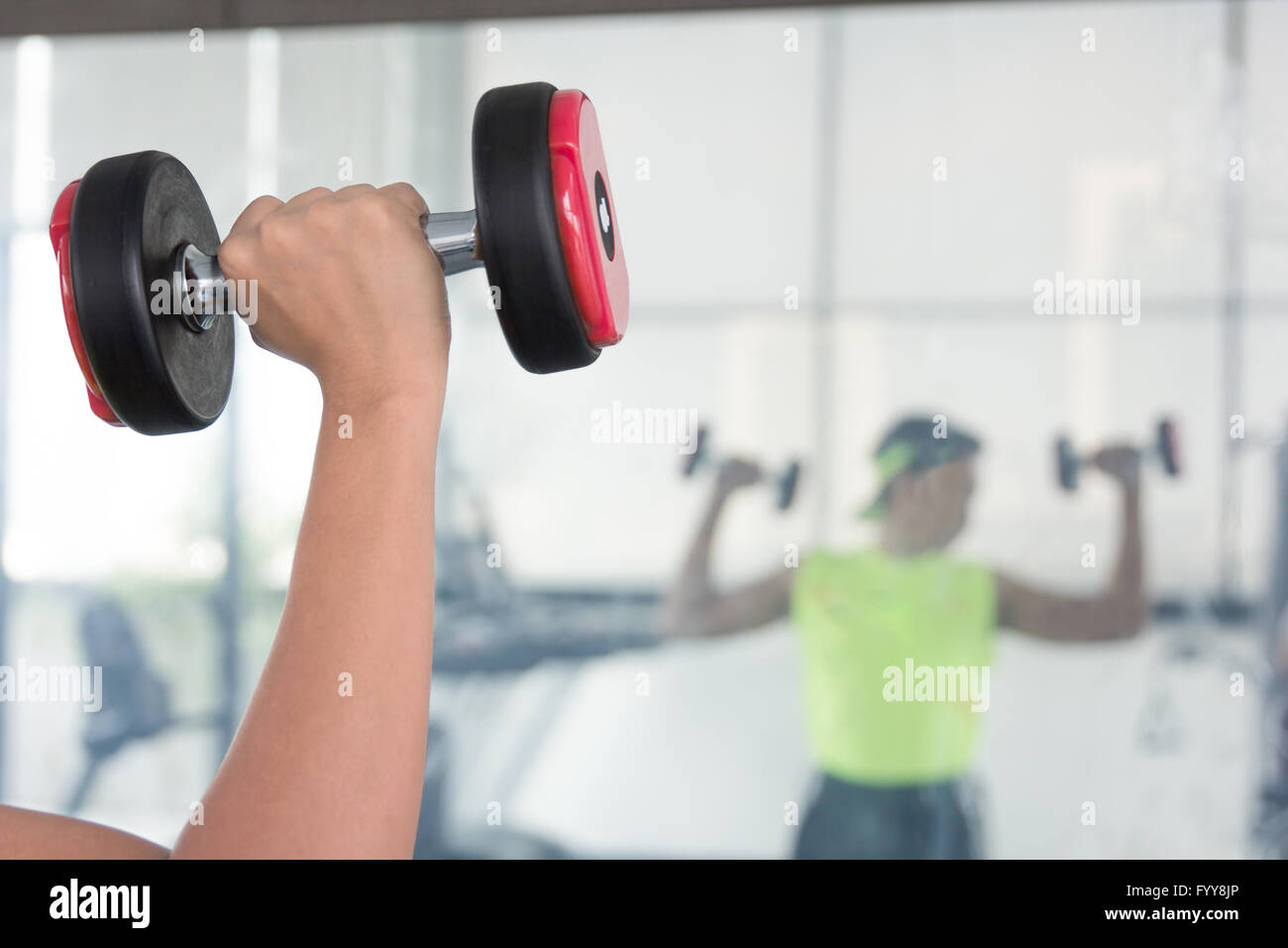 A young man watches arm muscle standing in front of the mirror as he performs a bicep curl with a chrome dumbbell Stock Photo