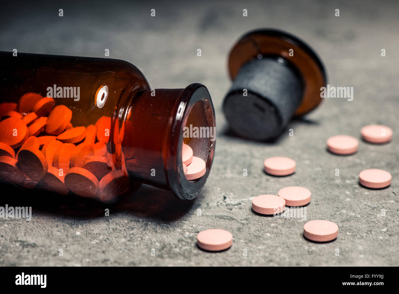 Glass bottle with pills spilled on stone table in close up. Concept of medicine, healthcare, addiction and treatment. Stock Photo
