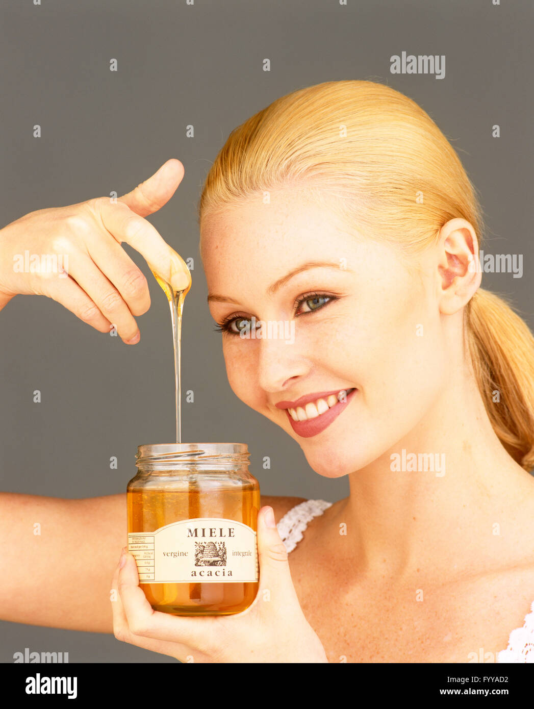 A blond woman holding Miele honey from the jar, inside. Stock Photo