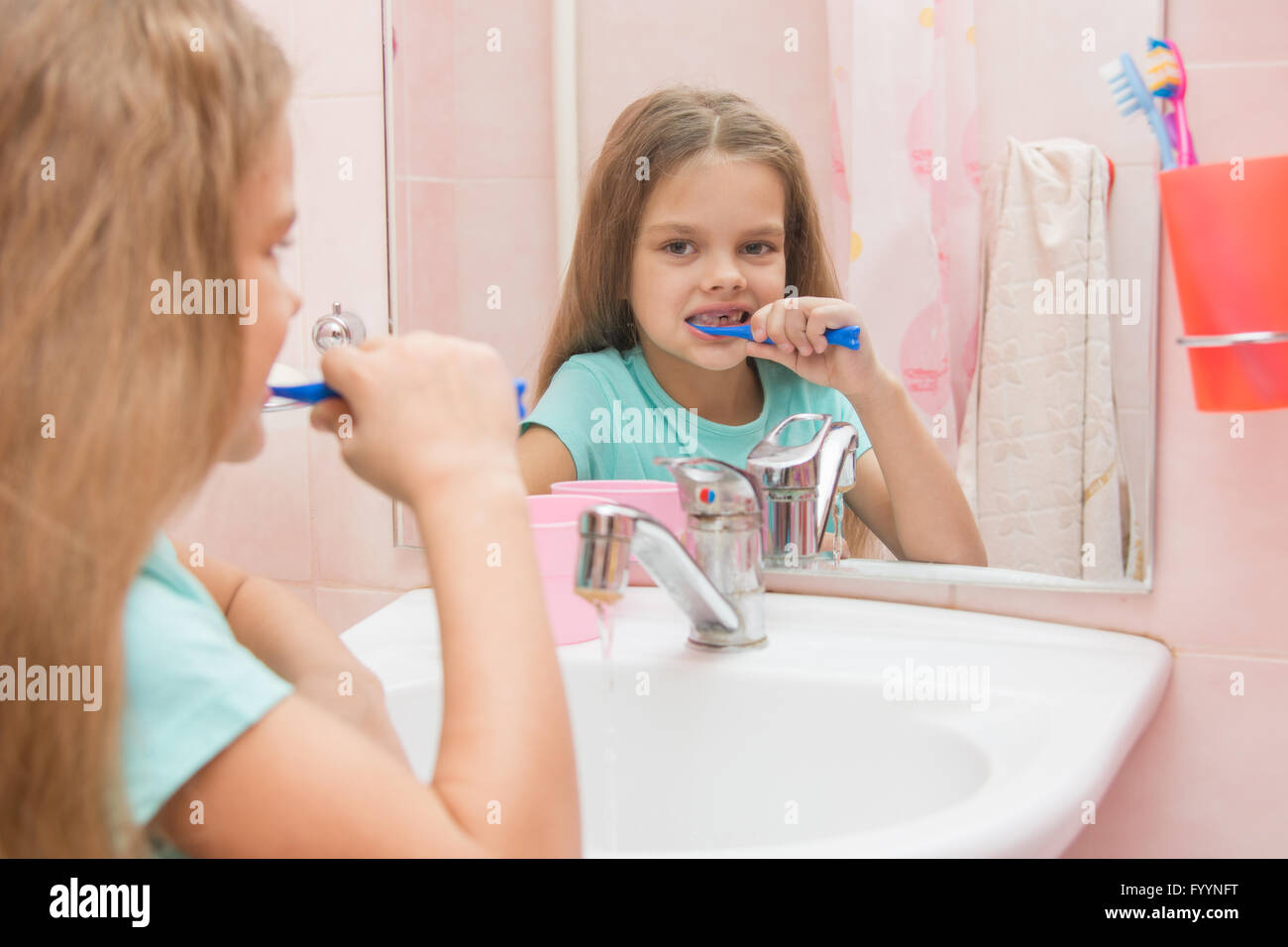 Six year old girl cleans teeth side looking in the mirror in the bathroom Stock Photo