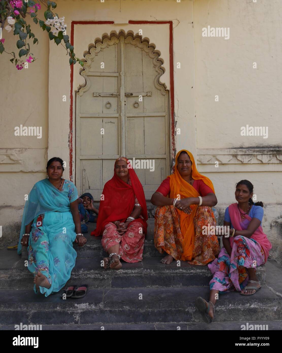 A group of Indian women, wearing the typical bright saris of Rajasthan, each in a different colour, sit smiling on some steps. Stock Photo