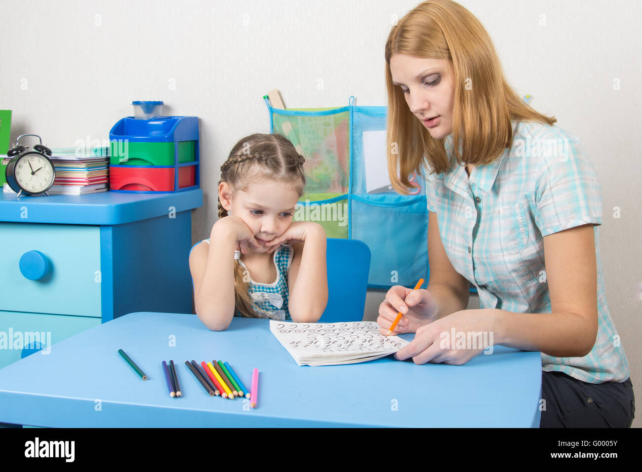 Five-year girl with interest looks at the teaching material explained by an adult Stock Photo