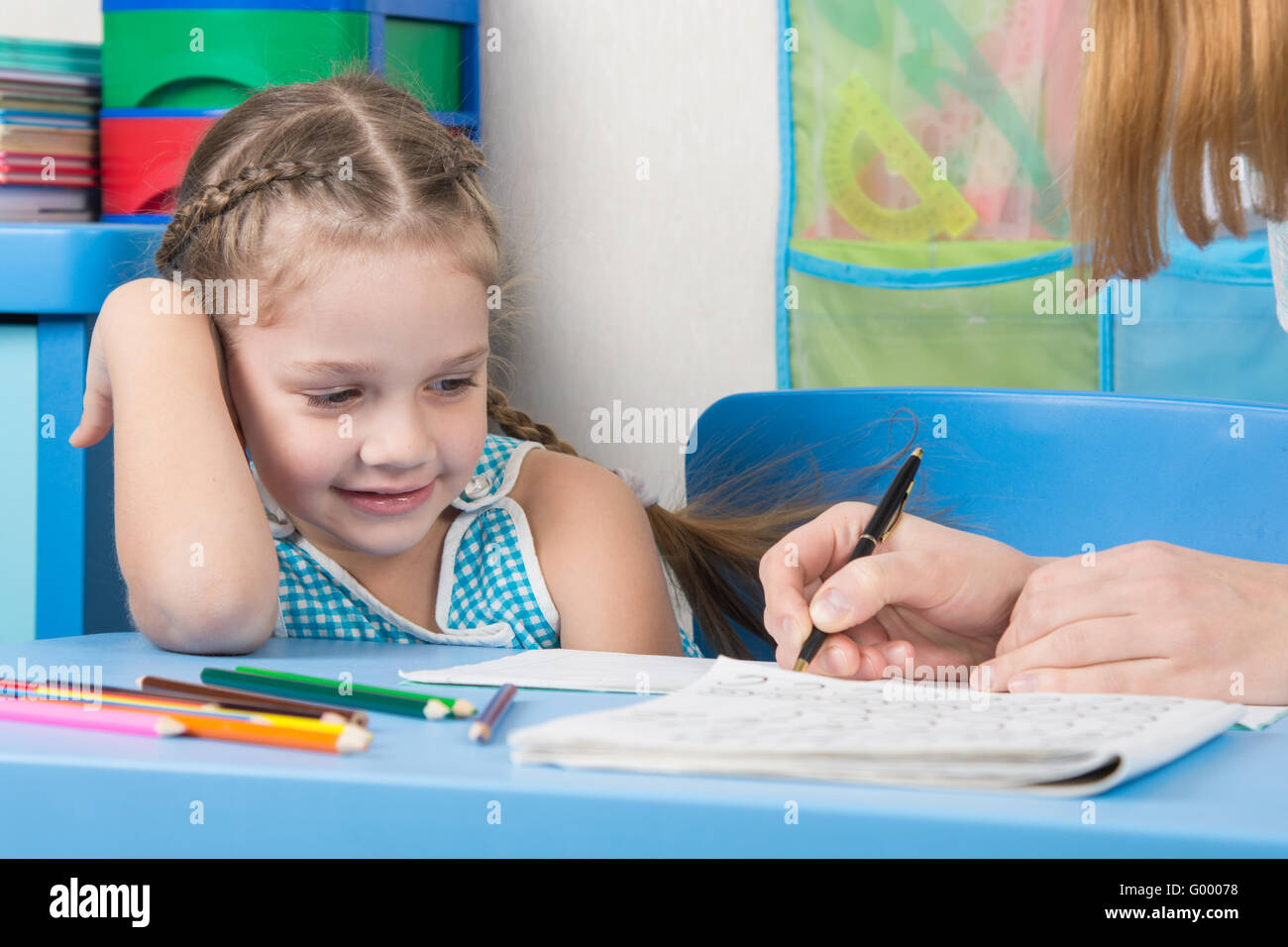 Five-year girl with a smile looking at my mother explaining how to write letters Stock Photo