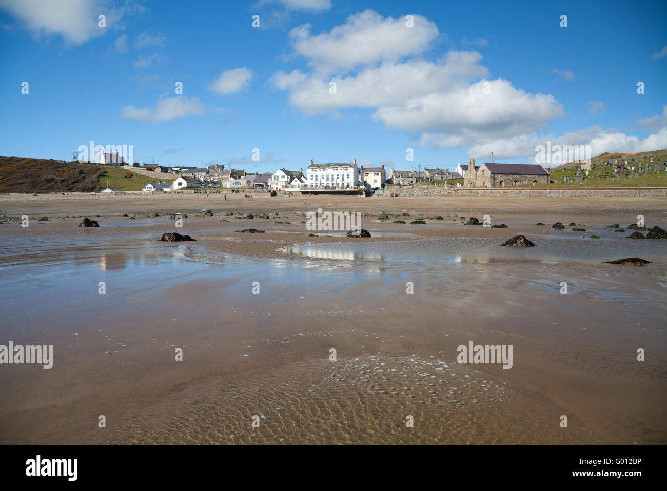 The view towards Aberdaron village (showing pub & church) taken from the beach at low tide on a summer spring day with blue sky Stock Photo