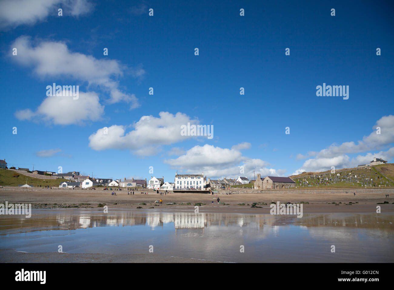 The view towards Aberdaron village (showing pub & church) taken from the beach at low tide on a summer spring day with blue sky Stock Photo
