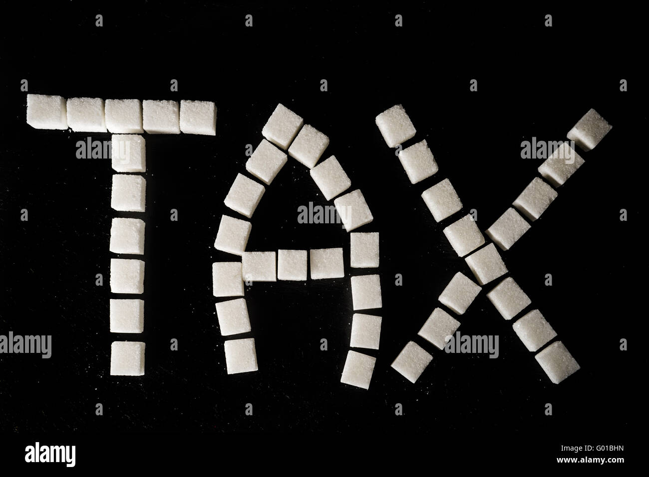 Word TAX made of white refined sugar cubes on black slate background, symbolising sugar tax Stock Photo