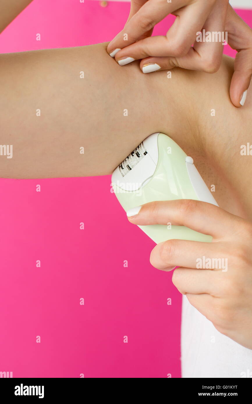 Woman epilates her armpit with an electric epilator device Stock Photo
