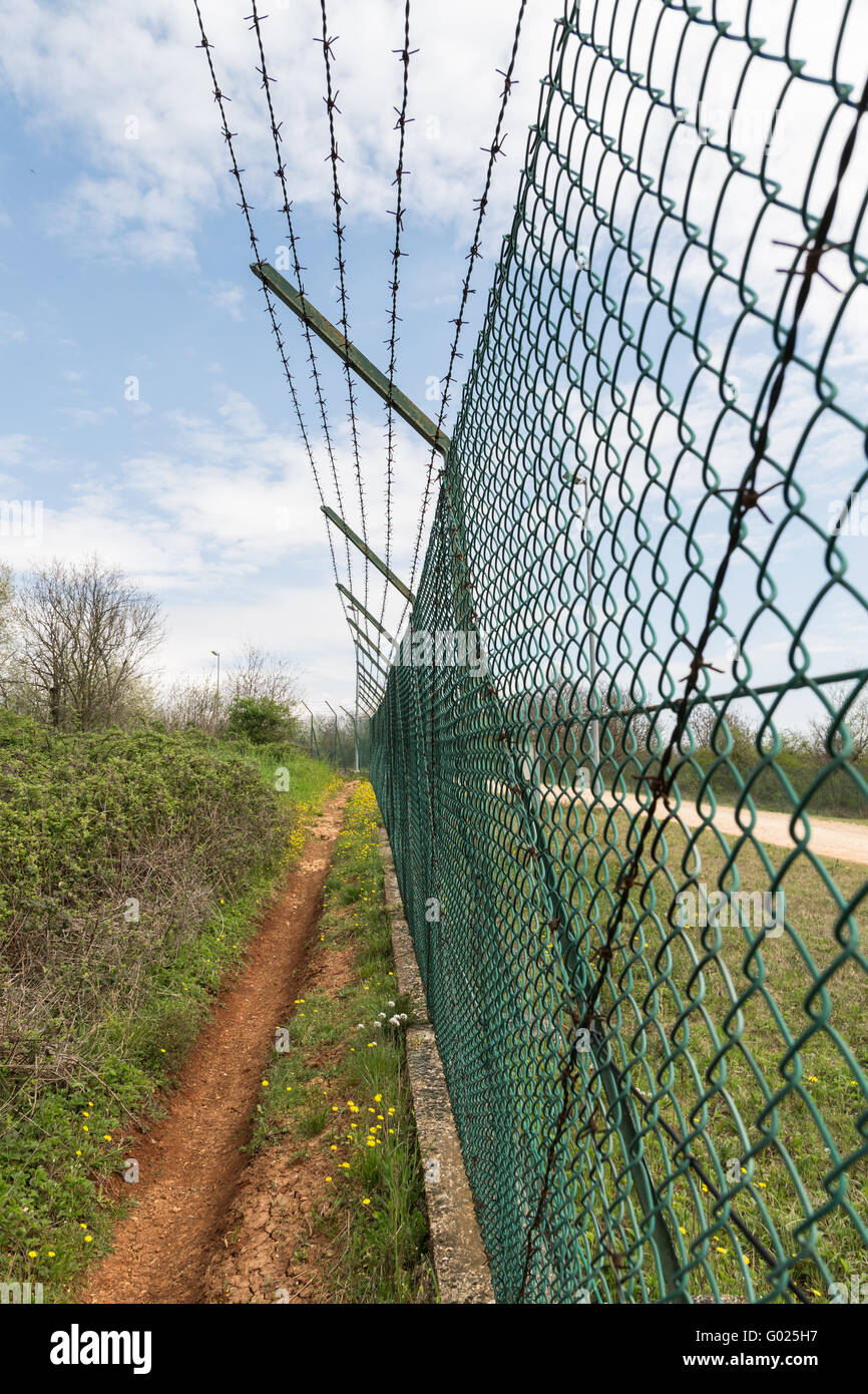 Green mesh fence topped with barbed wire. Stock Photo
