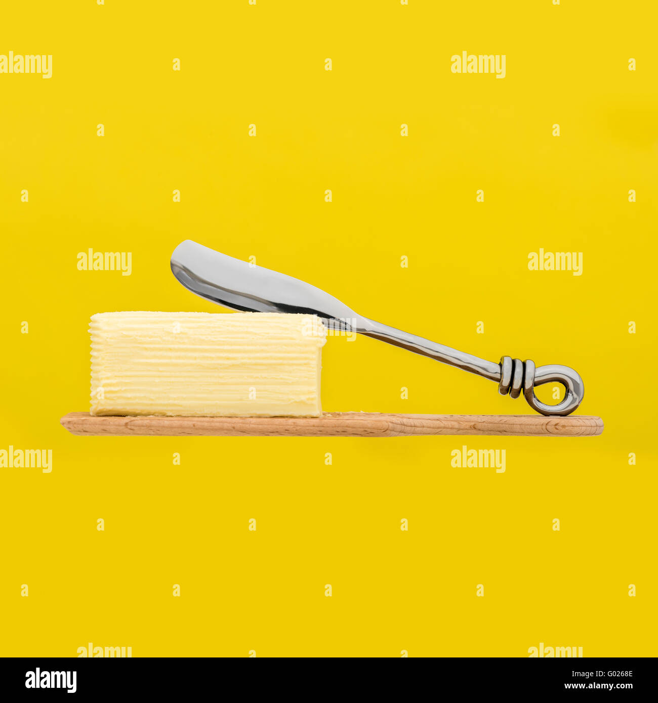 Hand churned homemade butter on wooden paddle with butter knife and yellow background. Stock Photo