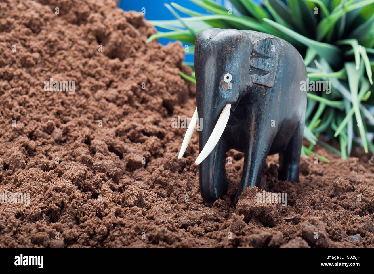 Wooden African elephant carving on sand with green plant and blue sky in the background Stock Photo