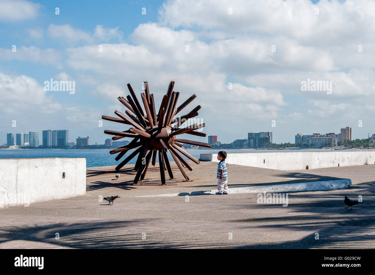 On the Puerto Vallarta malecon a small child contemplates Eriza-Dos, the iron sea urchin modern sculpture by artist Blu. Stock Photo