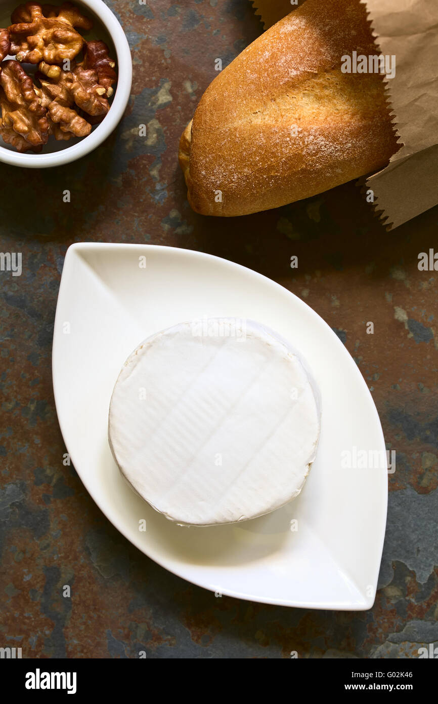Camembert cheese on small plate with baguette and walnuts on the side, photographed overhead on slate with natural light Stock Photo