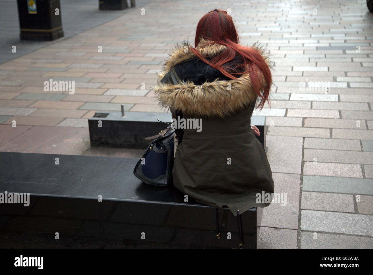 young girl with dyed red hair sitting on street bench Stock Photo